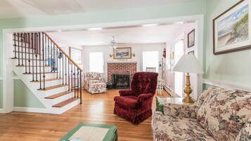 A spacious living room with a wooden staircase, a fireplace, and floral-patterned furniture.