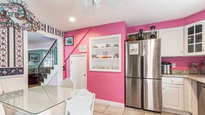 A kitchen with pink walls, white cabinets, a stainless steel refrigerator, and a glass-top dining table with white chairs.