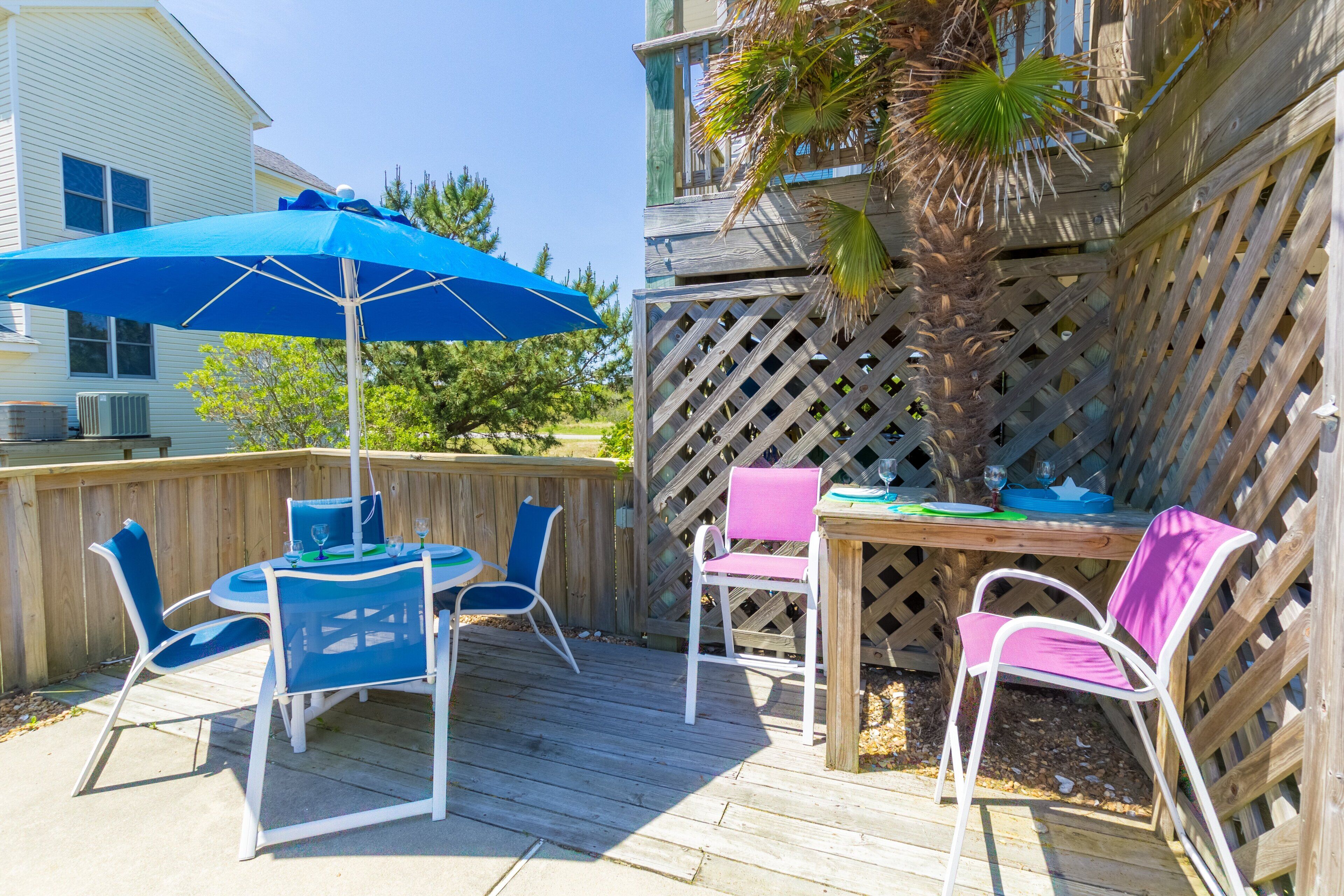 An outdoor patio with a wooden deck, a table with chairs, and a blue umbrella.