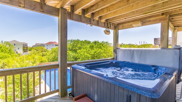 Eine Holzterrasse mit Whirlpool und Bank, mit Blick auf eine Wohngegend mit Häusern und Grünflächen.