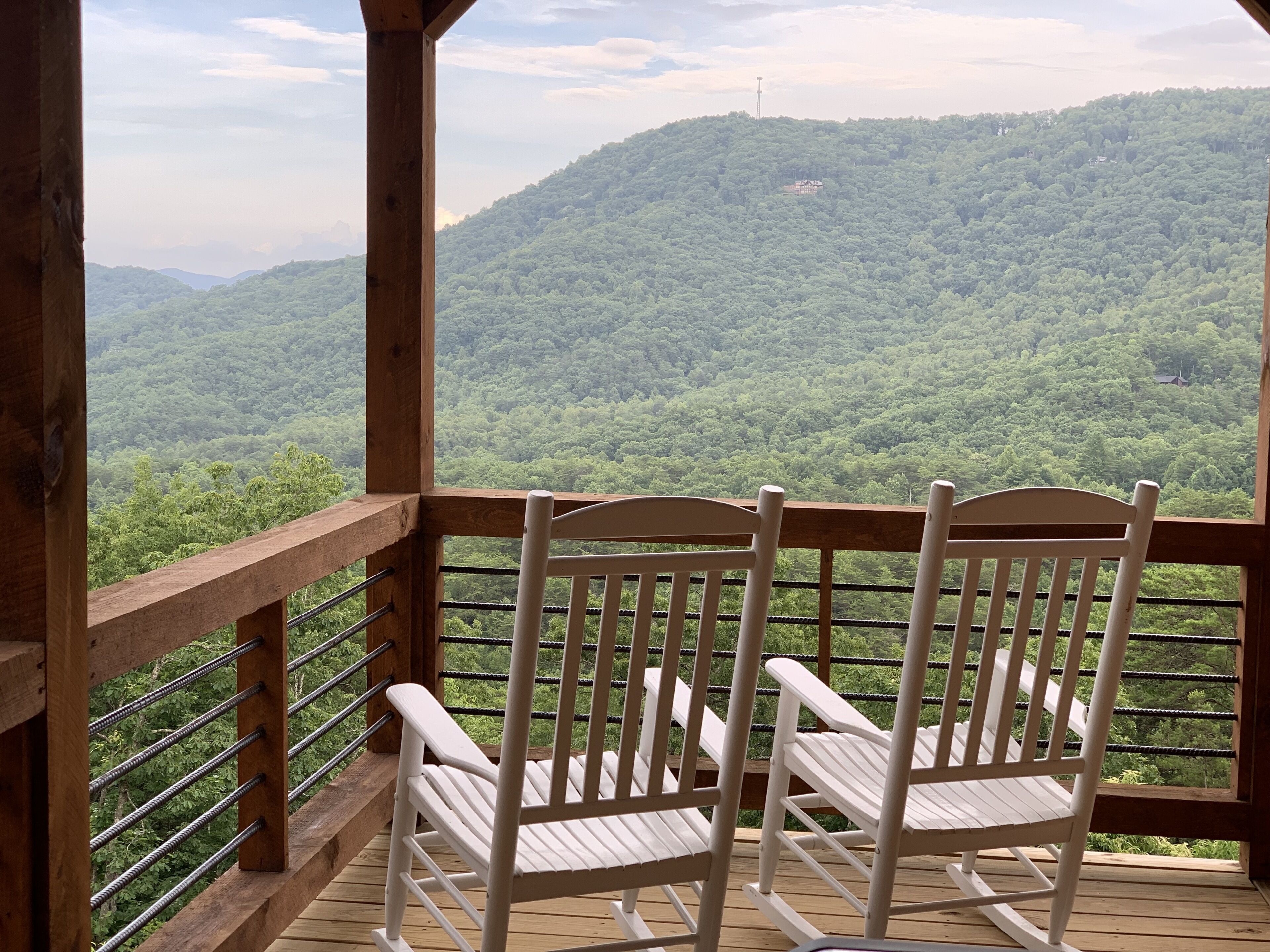 A wooden deck with two white rocking chairs overlooking a forested mountain.