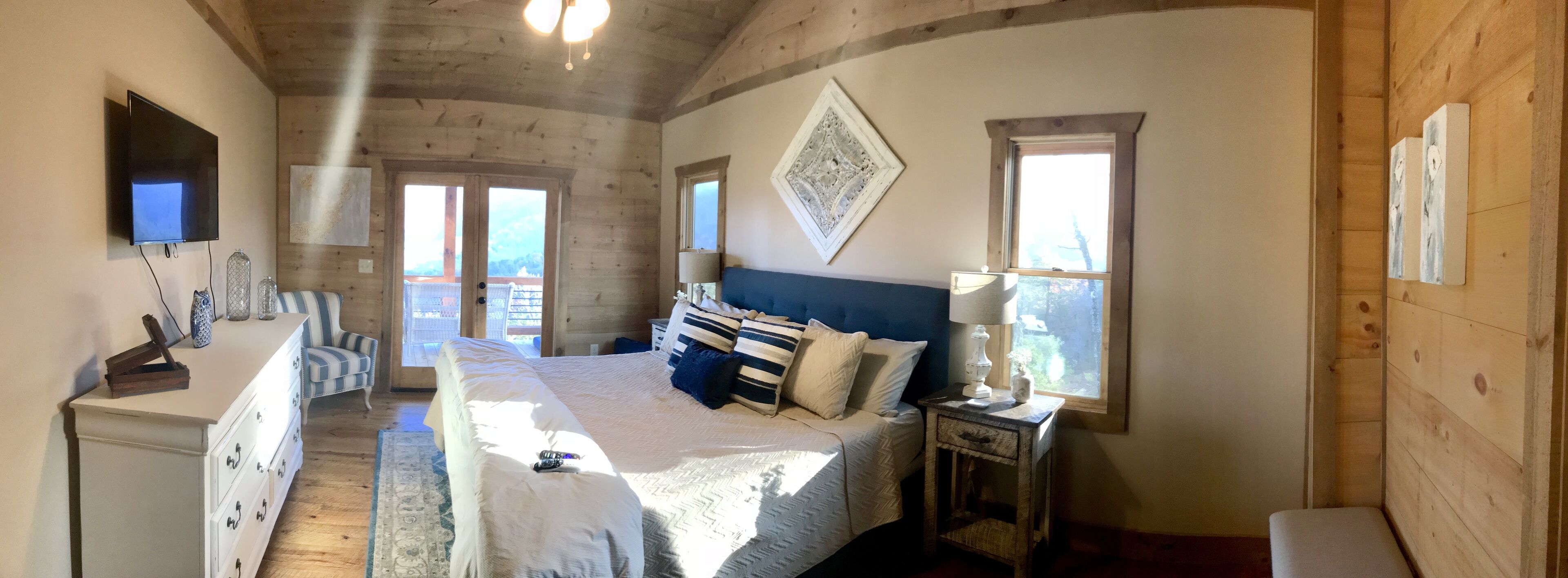 A bedroom with a bed, dresser, TV, and two windows.
