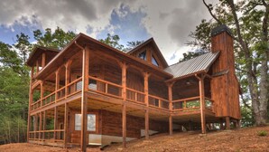 A large, multi-level wooden cabin with a prominent chimney, surrounded by trees. - Luxury cabin! Designer decorated.  Incredible views! Amazing sunrise! Secluded!  (Blue Ridge)