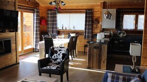 Un accogliente interno di una baita con zona pranzo, cucina, soggiorno con divano e televisione.