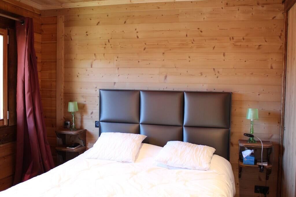 A wooden-paneled room with a bed, two nightstands, and a window with curtains.