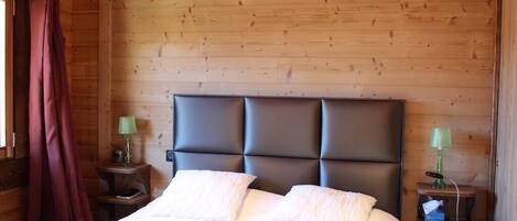 A wooden-paneled room with a bed, two nightstands, and a window with curtains.