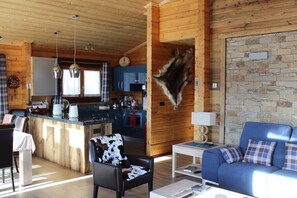 A cozy cabin interior with a wooden interior, a dining area, a kitchen, and a living room with a blue sofa and a mounted animal hide. - Chalet Llory, cosy and pleasant (Font-Romeu-Odeillo-Via)