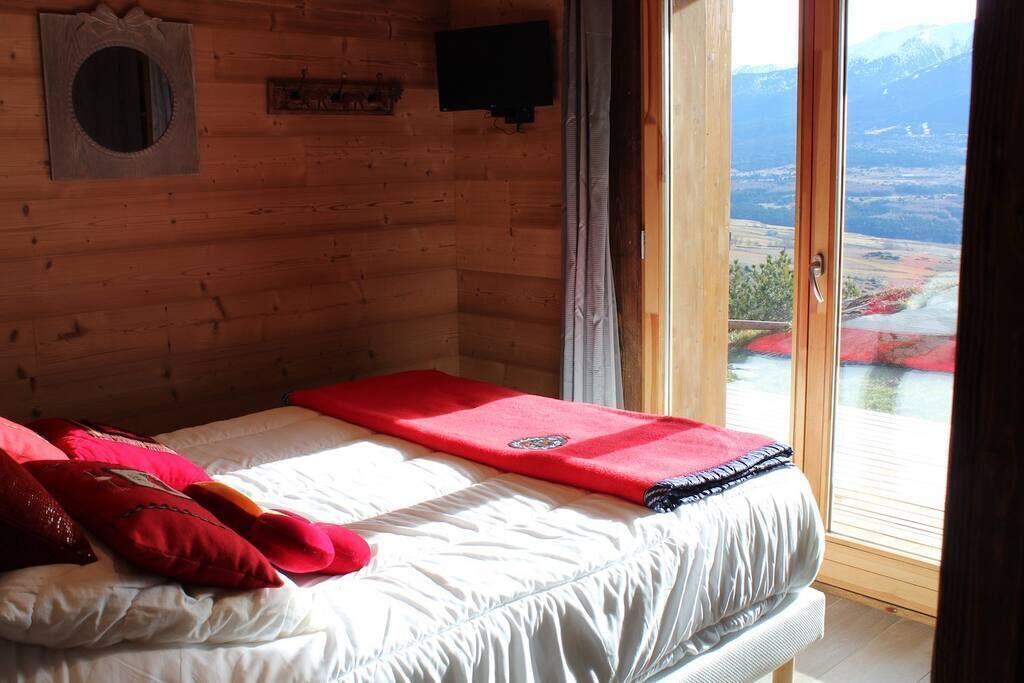 A wooden cabin room with a bed, a television, and a window with a view of a valley.