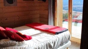 Una camera in una baita di legno con un letto, una televisione e una finestra con vista sulla valle.