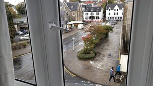 A view from a window overlooking a street with parked cars, a pedestrian, and buildings. - Portree Independent Hostel (Portree)