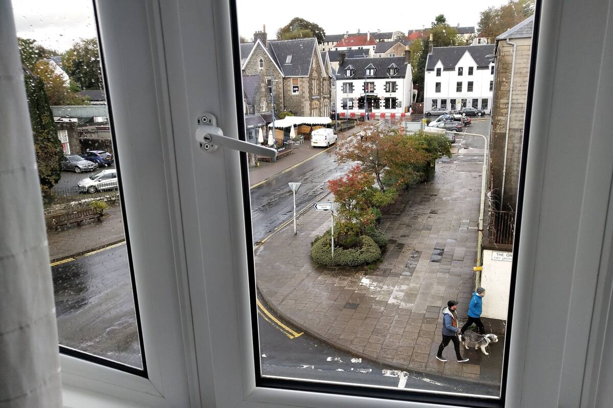 A view from a window overlooking a street with parked cars, a pedestrian, and buildings.