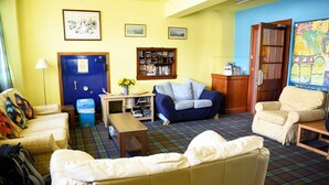A cozy living room with a sofa, armchairs, a coffee table, and a bookshelf. - Portree Independent Hostel (Portree)