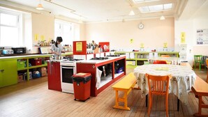 A kitchen with a stove, sink, and a person cooking. There are cabinets, a trash bin, and a table with chairs. - Portree Independent Hostel (Portree)