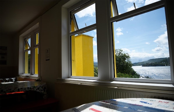 A room with large windows overlooking a body of water, a radiator, and a table with a patterned tablecloth.