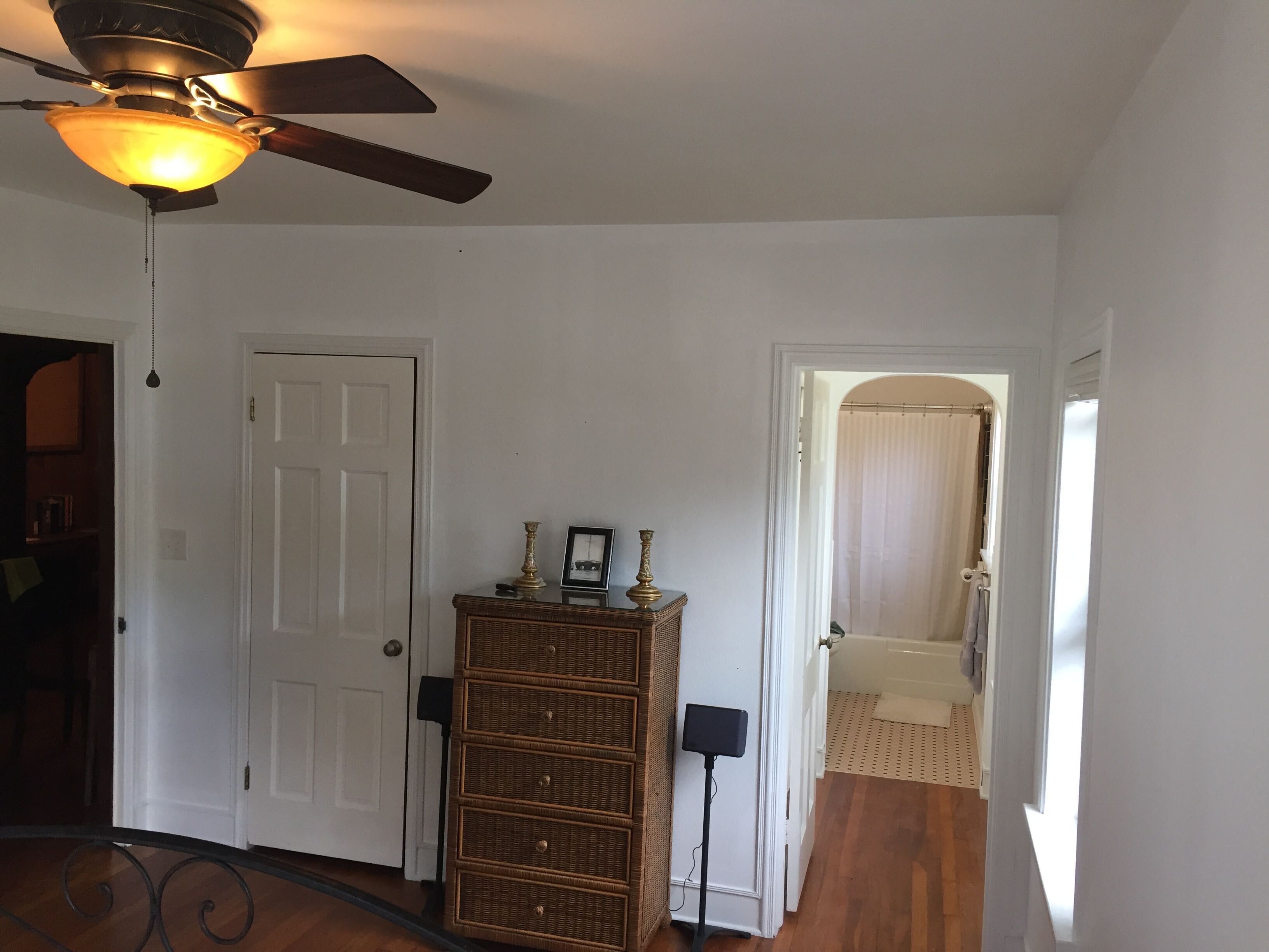 A room with a ceiling fan, a door, a wicker dresser, and a small table with decorative items.