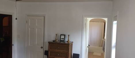 A room with a ceiling fan, a door, a wicker dresser, and a small table with decorative items.