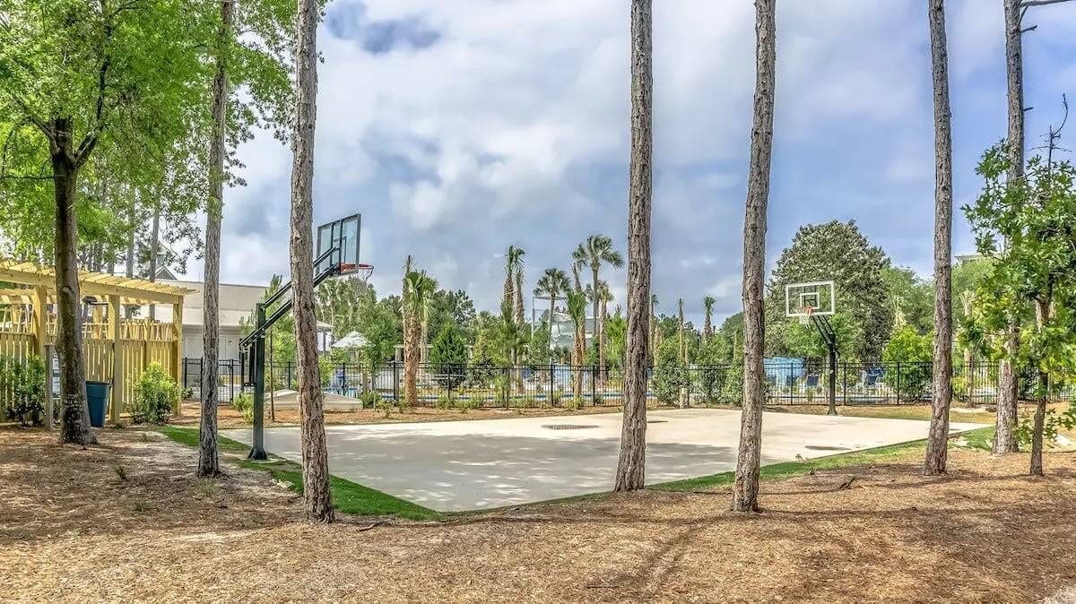 An outdoor basketball court surrounded by tall trees and a building with a yellow facade.