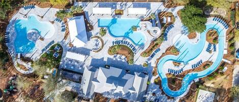 An aerial view of a resort with multiple swimming pools, a large building with a unique roof design, and surrounding landscaped areas.