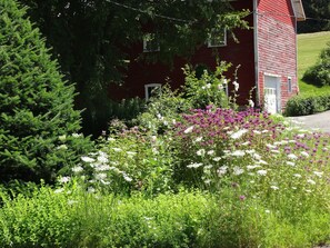 A red barn with a white door, surrounded by lush greenery and flowering plants.