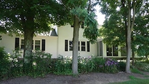 Een gebouw met twee verdiepingen, met een lichtgekleurde gevel, omringd door weelderig groen en bloeiende planten.