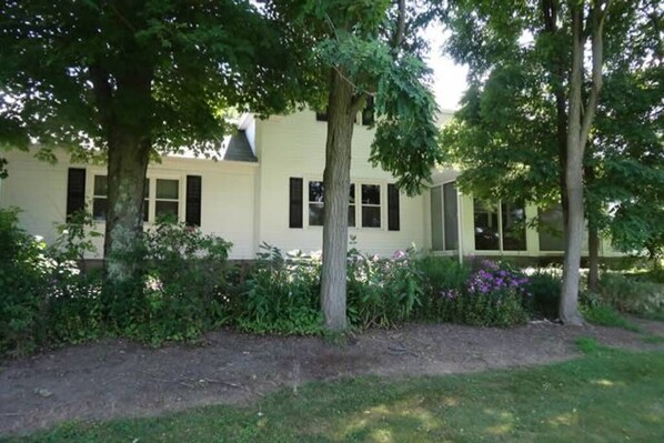 A two-story building with a light-colored exterior, surrounded by lush greenery and flowering plants.