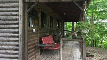 A rustic cabin with a covered porch, a red chair, and a table.