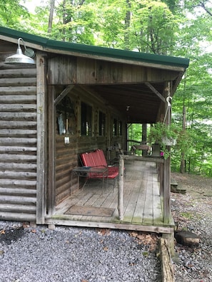 A rustic cabin with a covered porch, a red chair, and a table. - Cabin with lake views and beach access! (Trumansburg)