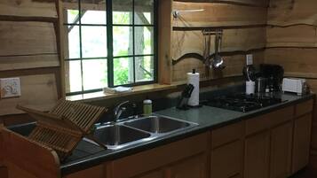 A wooden cabin kitchen with a large window, a sink, a stove, and wooden cabinets.