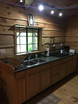 Cocina de cabaña de madera con un ventanal, un fregadero, una estufa y armarios de madera.
