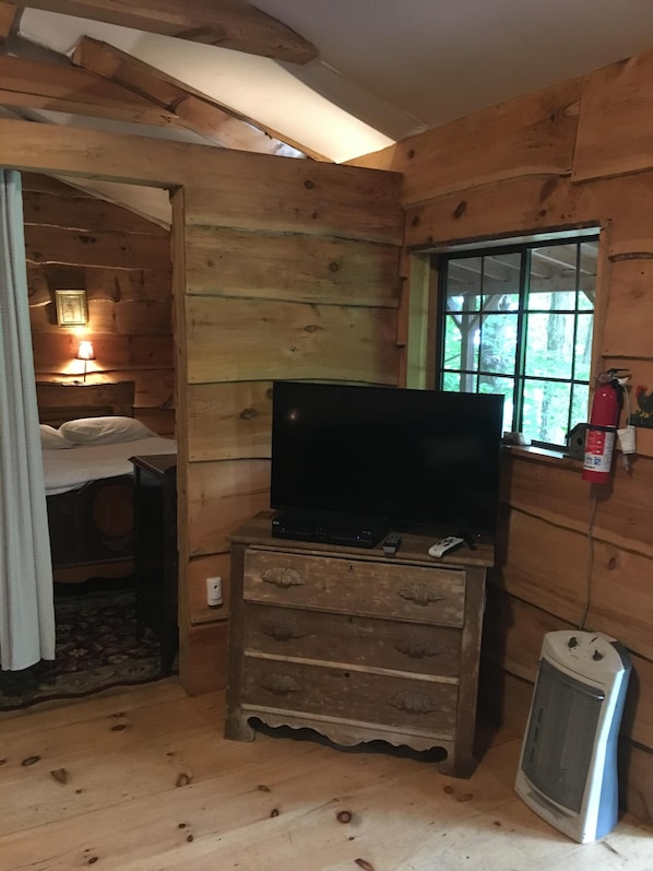 Une pièce de cabane en bois comprenant un lit, un téléviseur posé sur une commode, une fenêtre et un radiateur.