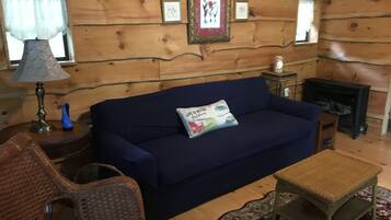 A cozy living room with a blue sofa, a small table, a wicker chair, and a fireplace.
