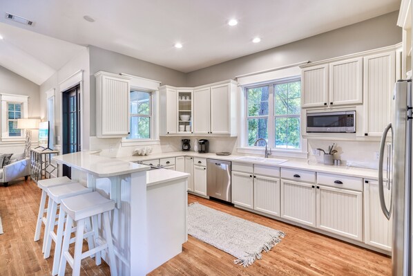 A modern kitchen with white cabinetry, a central island with stools, stainless steel appliances, and large windows providing natural light. - Upscale Coastal Hideaway w/ 4 Bikes, Pool Access, & Inviting Outdoor Living (Santa Rosa Beach)