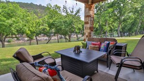 Un patio exterior con un pilar de piedra, muebles de mimbre y vistas a un lago y árboles.