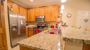 Una cocina con armarios de madera, un refrigerador de acero inoxidable, un microondas y una encimera de granito.