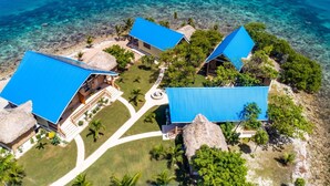 Une vue aérienne d’un complexe hôtelier comprenant plusieurs bâtiments, des eaux d’un bleu limpide et une pelouse bien entretenue.