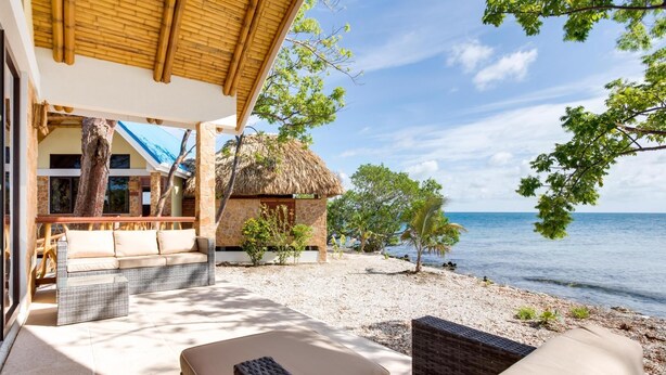 Une villa située en bord de mer, dotée d’une structure à toit de chaume, de meubles en osier et offrant une vue sur la mer.