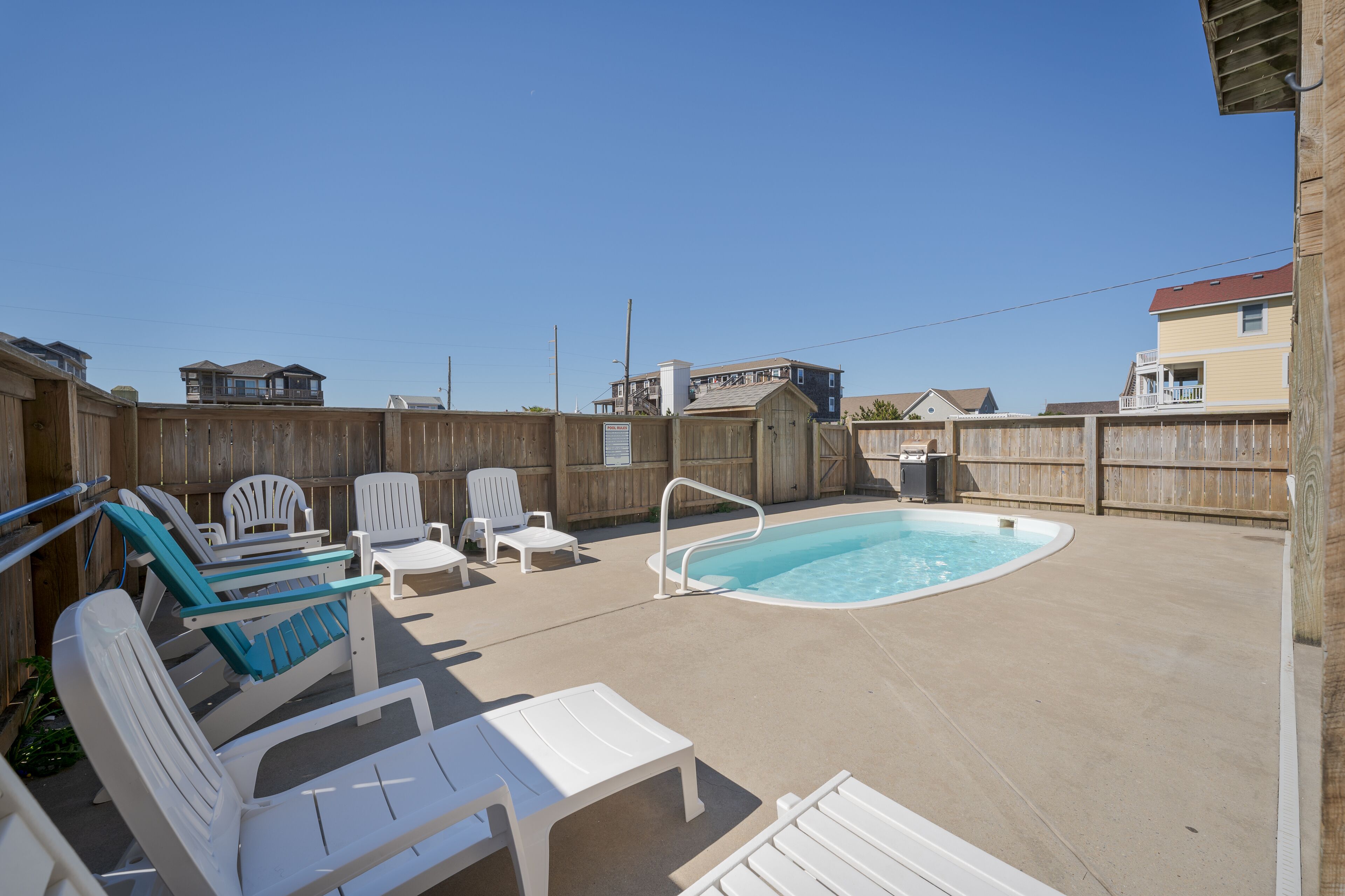 A backyard with a swimming pool, white lounge chairs, and a wooden fence.