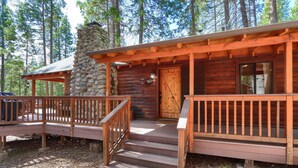 A log cabin with a stone chimney, wooden deck, and a porch with steps leading to the entrance.