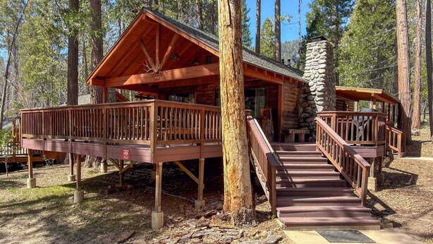 A wooden cabin with a stone chimney, wooden deck, and a staircase leading to the entrance.