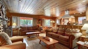 A cozy cabin interior with wooden ceilings, a fireplace, a sofa, a coffee table, and a dining area.