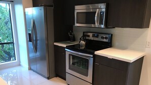 Une cuisine moderne équipée d’appareils électroménagers en acier inoxydable, notamment un réfrigérateur, un four à micro-ondes et un four traditionnel, et dotée d’une grande fenêtre qui laisse entrer la lumière naturelle.