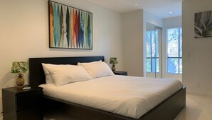 Une chambre à coucher moderne avec un grand lit, deux tables de chevet et un tableau abstrait aux couleurs vives accroché au-dessus du lit.