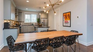 Une cuisine moderne avec une table à manger en bois et des chaises noires, un lustre et une affiche accrochée au mur.