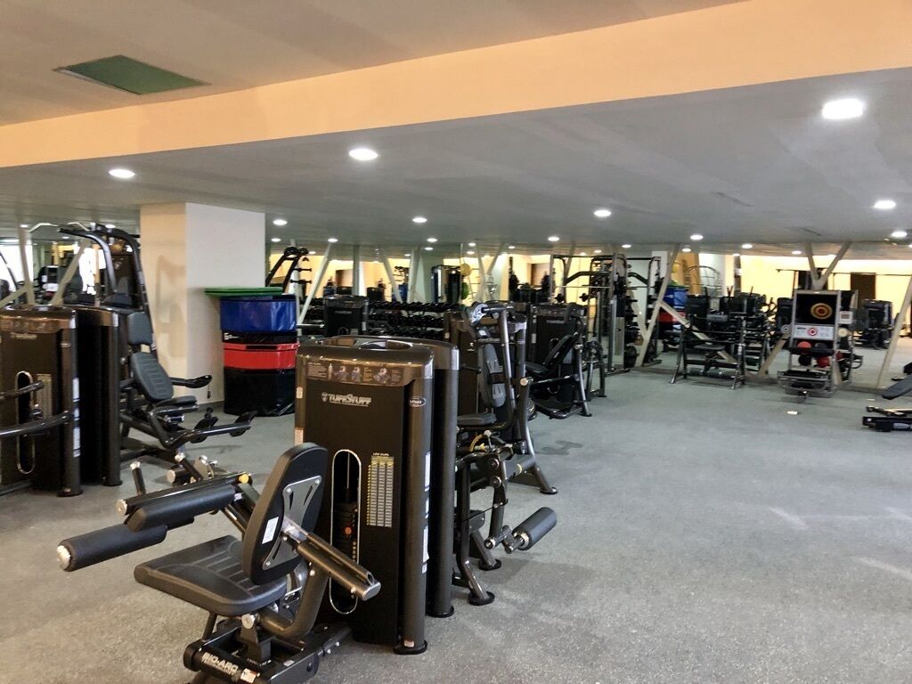 Un gimnasio con diversas máquinas de ejercicio, espejos y un ambiente limpio y bien iluminado.