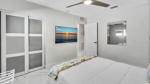 A bedroom with a bed, a ceiling fan, a wall-mounted TV, and a sliding door. - 2BR Hot Tub Oasis - 2 Mi FLL, 4 Mi Beach, Sleeps 6 (Dania Beach)