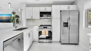 A modern kitchen with white cabinets, stainless steel appliances, a dishwasher, and a large window. - 2BR Hot Tub Oasis - 2 Mi FLL, 4 Mi Beach, Sleeps 6 (Dania Beach)