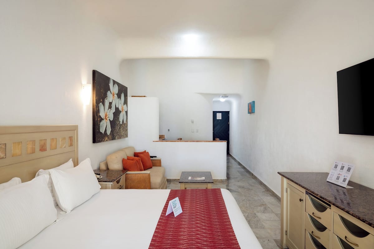 A hotel room with a bed, a desk, a chair, a small table, a sofa, and a painting on the wall.