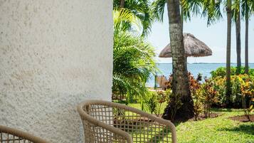 Wicker chairs with cushions, a thatched umbrella, and a view of the sea with palm trees.