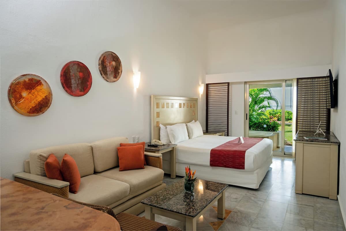 A hotel room with a bed, a sofa, a small table, a nightstand, and wall art.