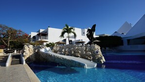 En swimmingpool med en stenvæg og en palme, omgivet af moderne bygninger.